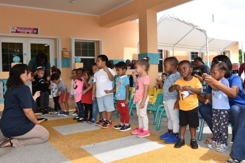 Teacher in Cayman Brac kneels and talks to students outside.
